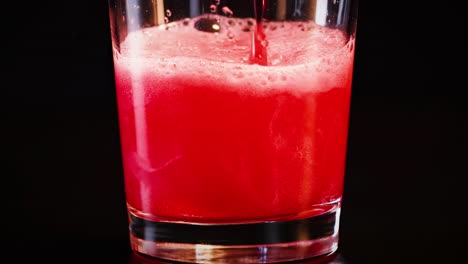 a sequence showing a red beverage fizzing and bubbling in a glass against a dark background.