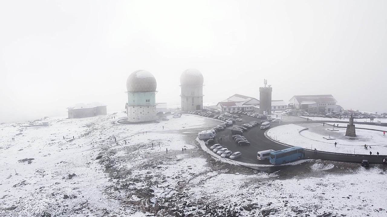 Serra da Estrela mountain summit Torre covered in snow during winter, featuring a radar station, telecommunications towers, and surrounding infrastructure shrouded in thick fog, drone orbit