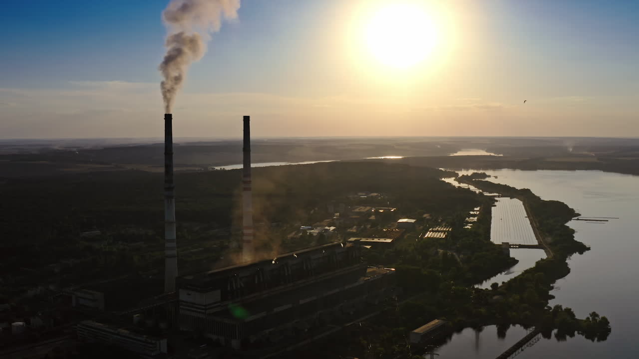 Dark silhouette of a factory at sunset. Manufacture releases harmful smoke into the air. Nature in danger. Industrial plant near the river in the evening.