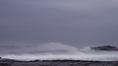 fuertes vientos marinos levantan el borde de las olas rompiendo en las rocas en cámara lenta