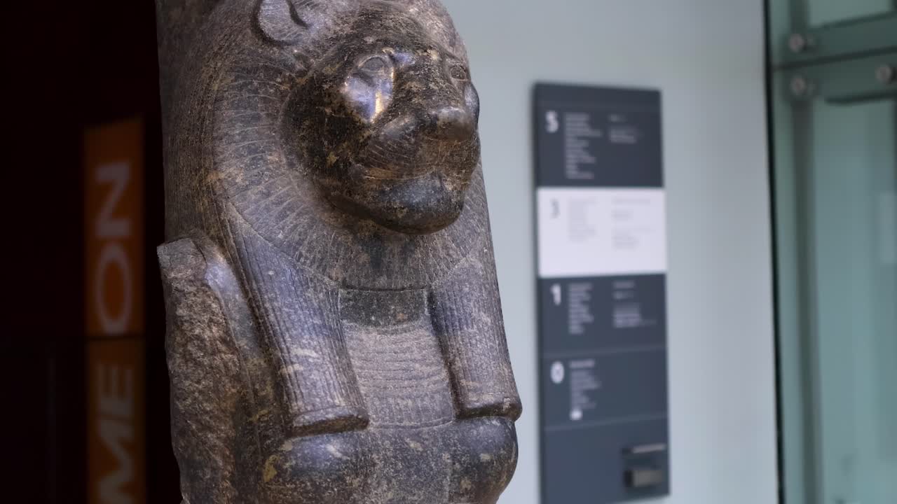 Detailed view of a lioness-headed statue with visible museum signage and modern interior elements.