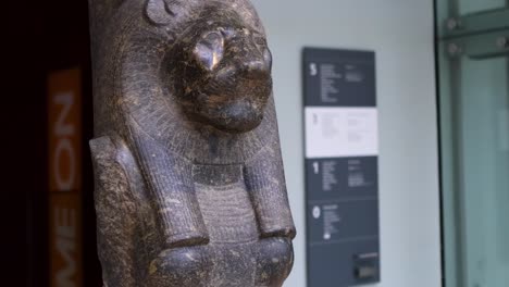 detailed view of a lioness-headed statue with visible museum signage and modern interior elements.