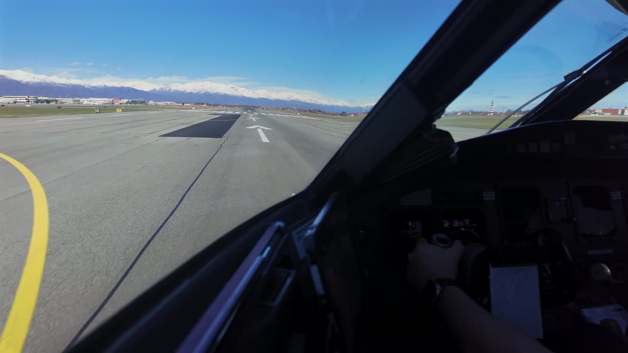 Prospettiva immersiva del pilota dall'interno di una cabina di pilotaggio di un jet che inizia la corsa di decollo da una pista corta vicino alle Alpi.