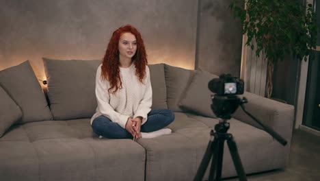 attractive curly redhead young girl vlogger is talking in front of camera recording video for online blog in internet