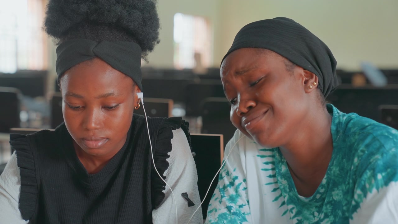 Madre afroamericana e hija estudiando juntas, pupitre de aula, rostros concentrados, madre guiando a la niña con la tarea, expresiones de concentración, apoyo suave, pañuelo en la cabeza, luz natural.