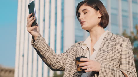 Stilvolle-Frau,-Die-Ein-Smartphone-Benutzt-Und-Kaffee-In-Der-Hand-Hält,-Um-Ins-Freie-Zu-Gehen.