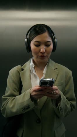 woman in elevator using phone and headphones