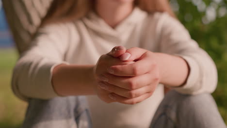 joven se sienta con las manos juntas, expresando calma e introspección en medio de un fondo borroso de vegetación exuberante y una figura débil en azul