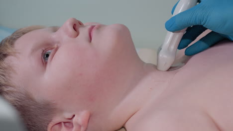 close up of young boy lying calmly while female medical professional in blue gloves performs throat ultrasound examination using transducer with gel during clinical diagnostic procedure in a hospital