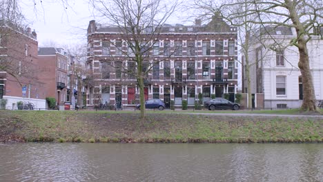 a three-storey important brickwork building, with traffic driving in front, seen from across the flowing canal in utrecht, the netherlands