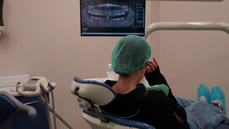 rear shot of a young female patient sitting in a dental chair with an x-ray picture of her teeth waiting for the doctor