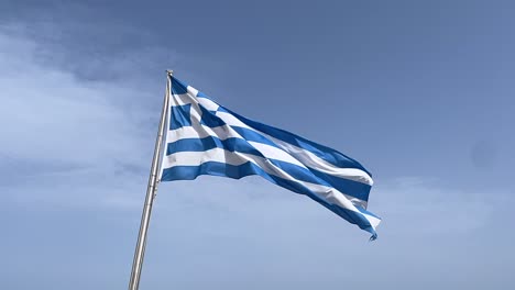 cinematic greek flag on pole waves in the wind, slow motion, blue sky, clouds