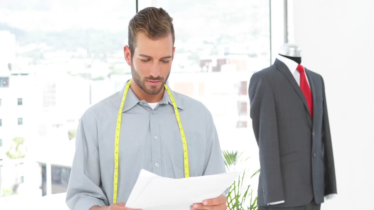 diseñador de moda guapo mirando bocetos y trajes en maniquí