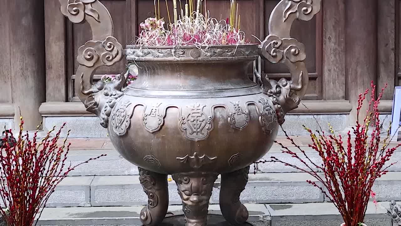 A detailed view of a traditional bronze incense burner flanked by red floral arrangements