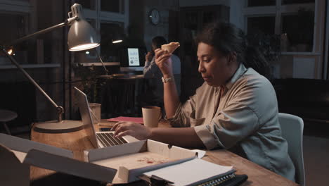woman working late in office eating pizza and drinking coffee