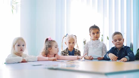 group of little students at a circle table during the lesson. children learning english together in games at primary school.