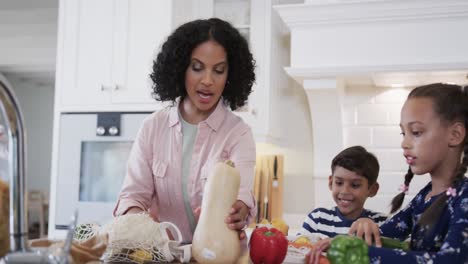 Happy-biracial-father,-mother,-son-and-daughter-unpacking-shopping-in-kitchen,-slow-motion