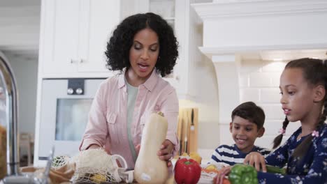 happy biracial father, mother, son and daughter unpacking shopping in kitchen, slow motion