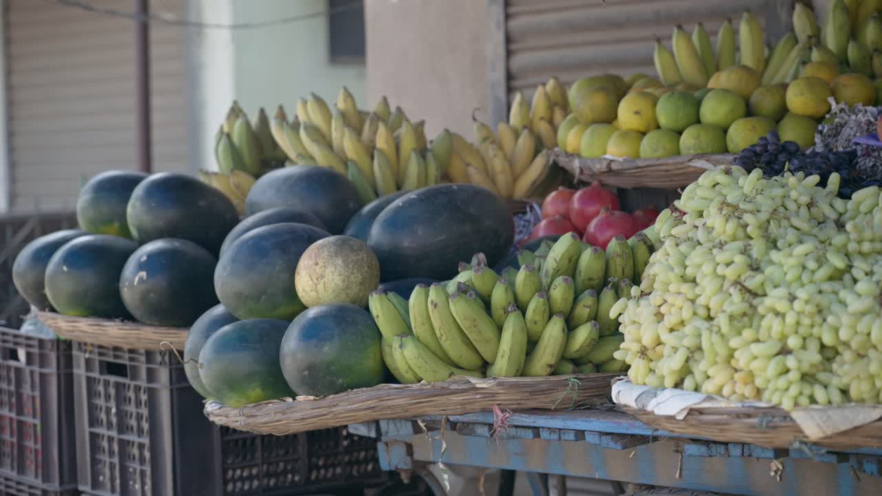 Una vivace bancarella di mercato all'aperto con mucchi di angurie, banane, uva e agrumi. Ideale per documentari di viaggio, contenuti sullo stile di vita sano e temi sul commercio locale.