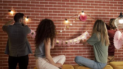 friends preparing party indoors hanging garlands and hbirthday letters