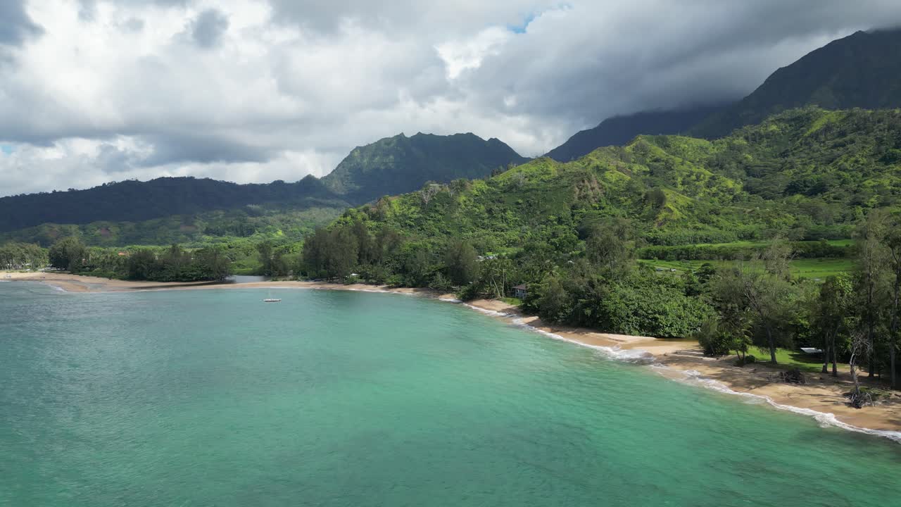 Drone video of turquoise coastline at Hanalei Bay, Kauai, Hawaii—lush forest and dramatic mountain backdrop meet clear tropical waters in this vibrant aerial of island paradise
