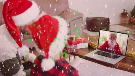 Animation-of-snow-falling-over-caucasian-man-with-his-son-in-santa-hats-on-laptop-video-call