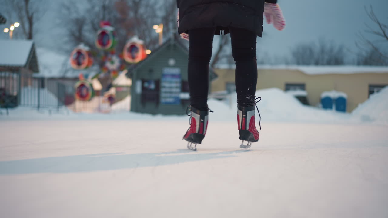 Closeup of person skating on outdoor rink in winter evening, red skates gliding over frozen surface, snow and festive decorations visible in background, capturing seasonal activity with energy and motion