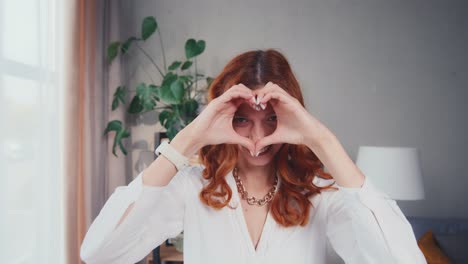 happy redhead woman making shape heart gesture with hands on eve of valentine