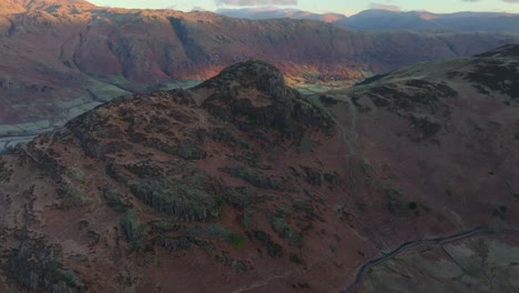 flying towards craggy mountain shoulder with pan up revealing mountain peaks with dawn light and valley floor. langdales, english lake district, cumbria, uk.