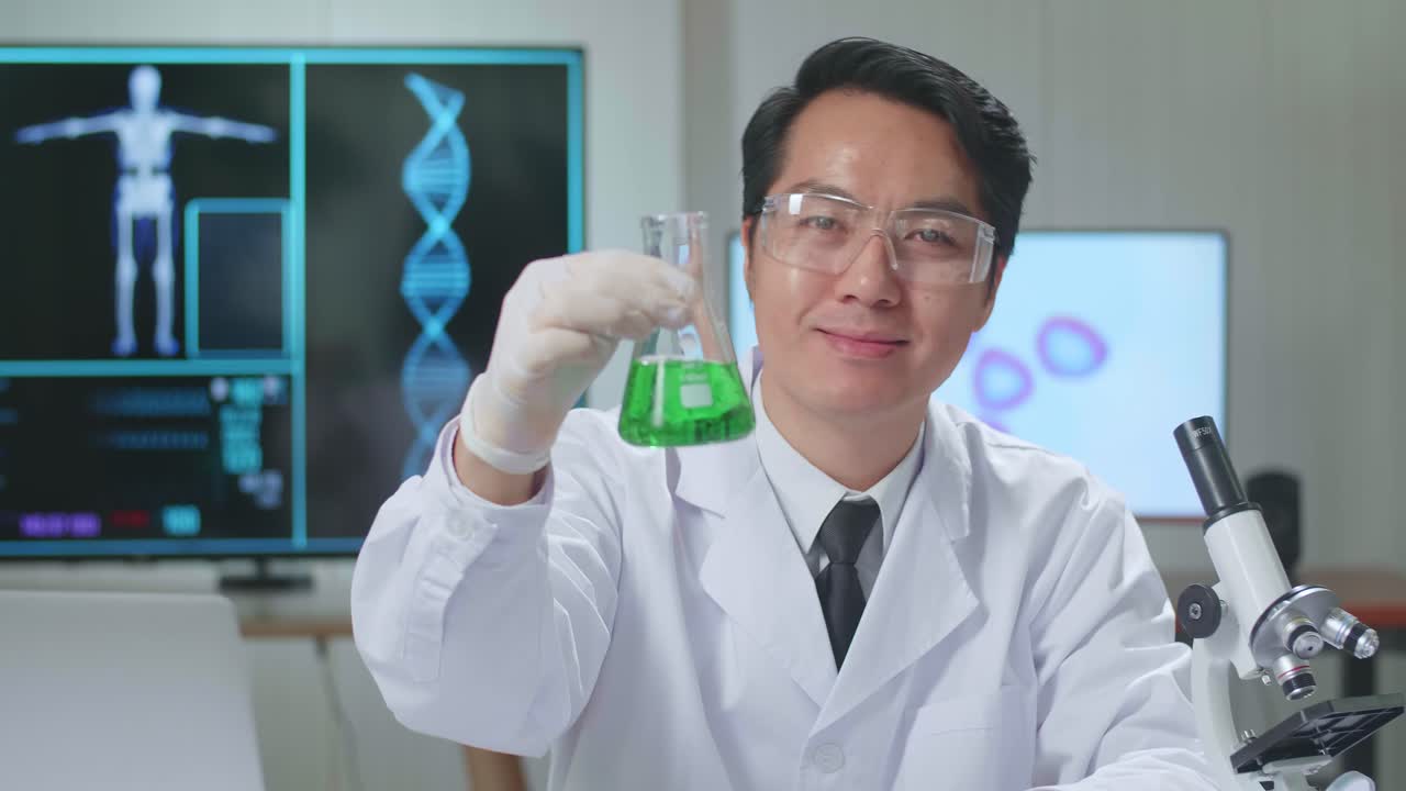 Young Asian Male Research Scientist Looking  Glass Test Tube And Warmly Smiles Into The Camera