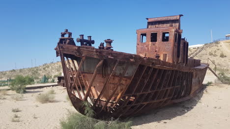 Rusty-Abandoned-Ship-in-Sand-of-Former-Aral-Lake,-Corroded-Remains-of-Vessel-on-Hot-Sunny-Day