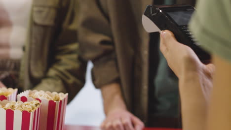 primer plano de una mujer irreconocible que paga con el teléfono en el mostrador de boletos en la sala de cine