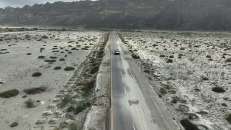 imágenes de seguimiento de aviones no tripulados de un coche jeep desde el frente en una carretera recta entre el valle y la montaña hingol baluchistan