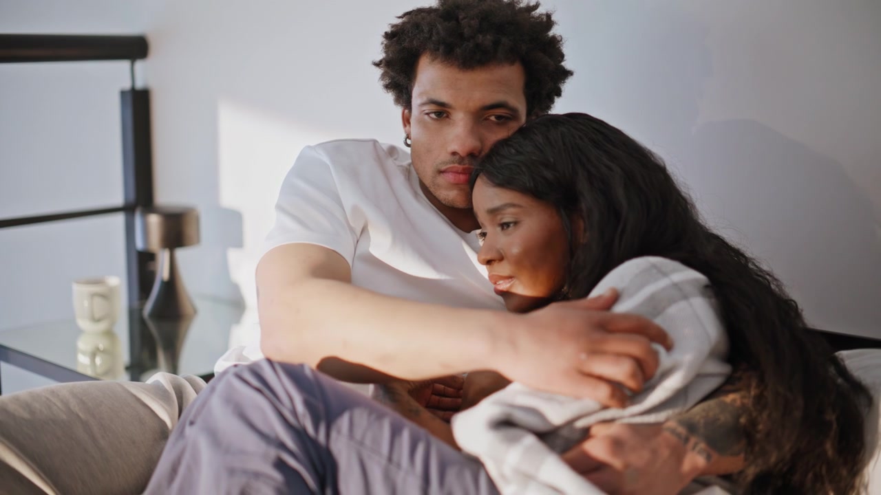 Upset couple cuddling together sharing problems in bedroom closeup. Young family