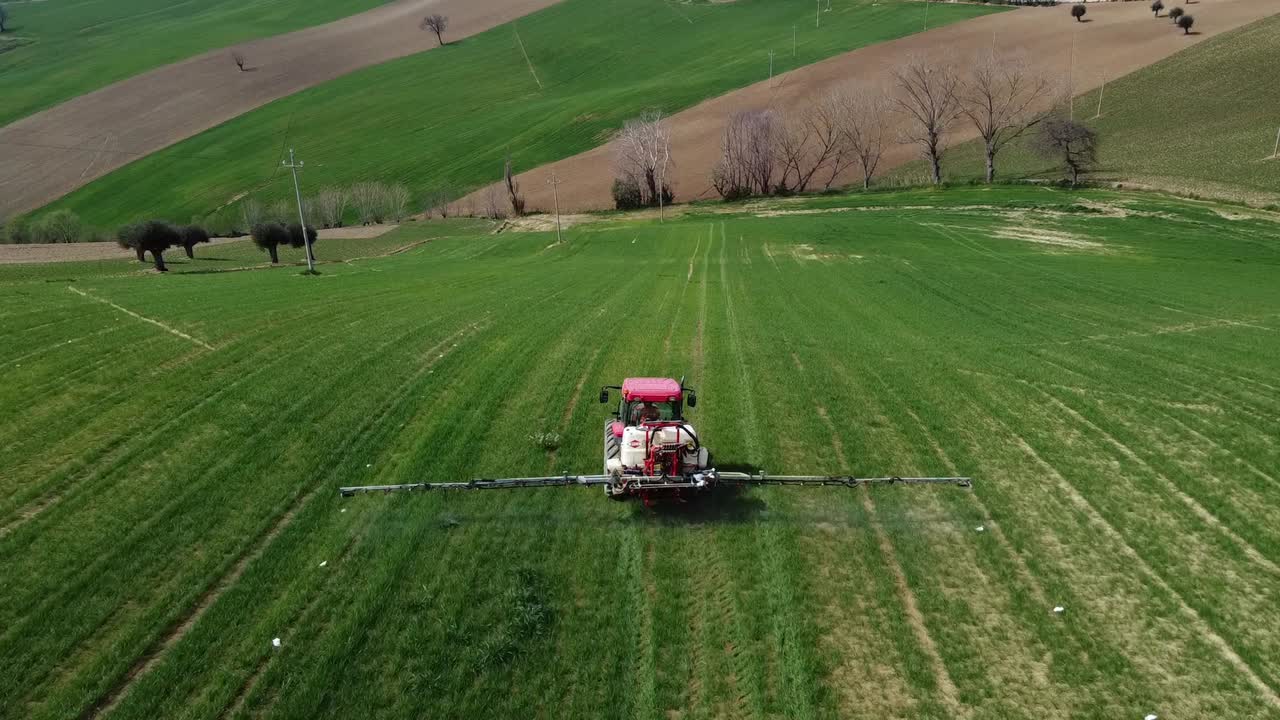 Aerial view of following farming tractor spraying on field with sprayer, herbicides and pesticides insecticide to the green field plowed land