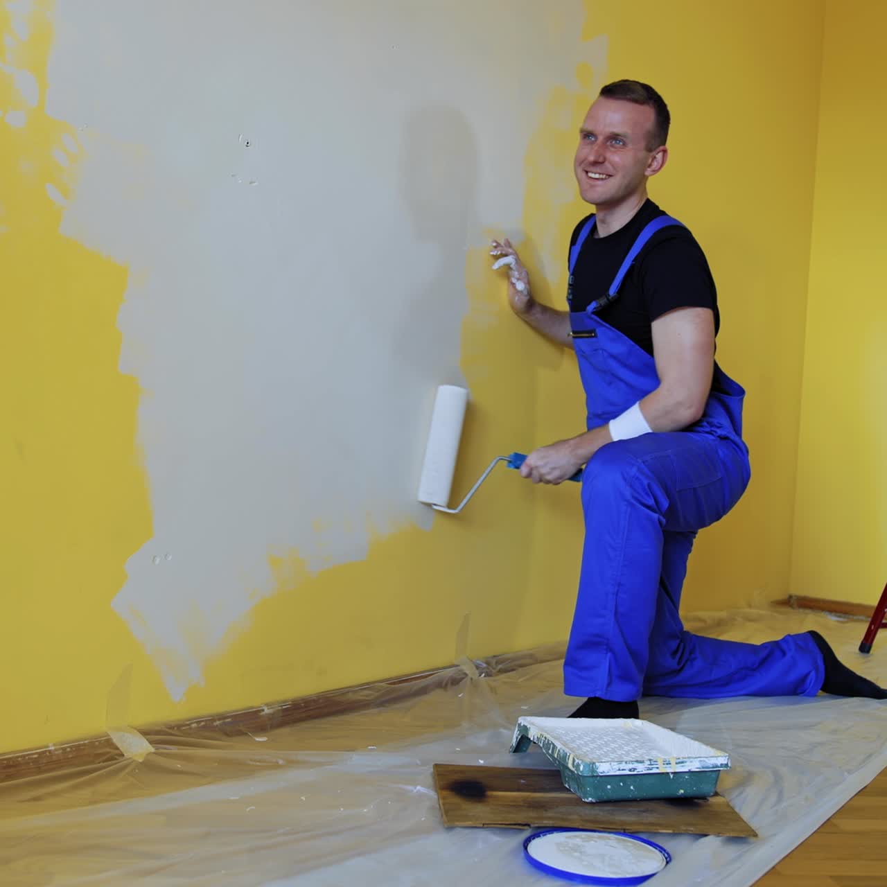 Happy male worker is painting wall. Professional young man with paint roller having fun in the apartment. Room painting job. Renovation home concept