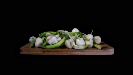 push in shot of fresh white onions over a wooden cutting board on black background at eye level