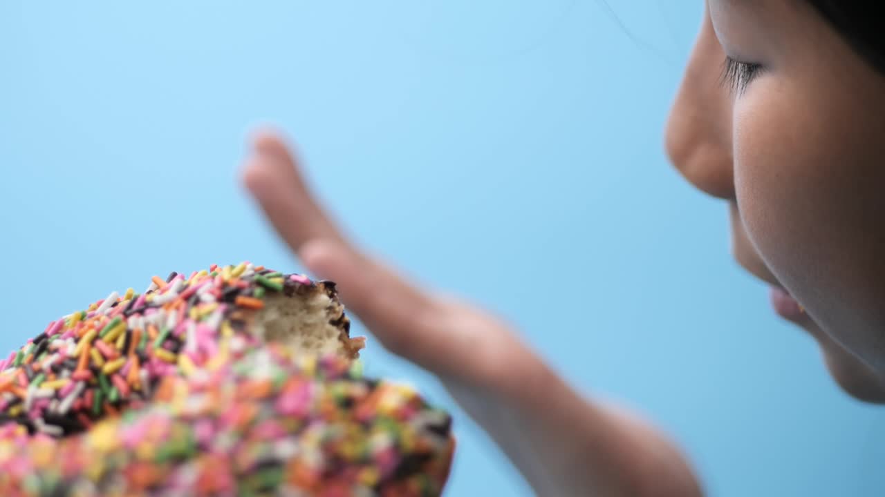 아시아 소녀가 초콜릿 도을 먹고 있습니다. 파란색 배경, 측면 뷰, 느린 동작으로요.