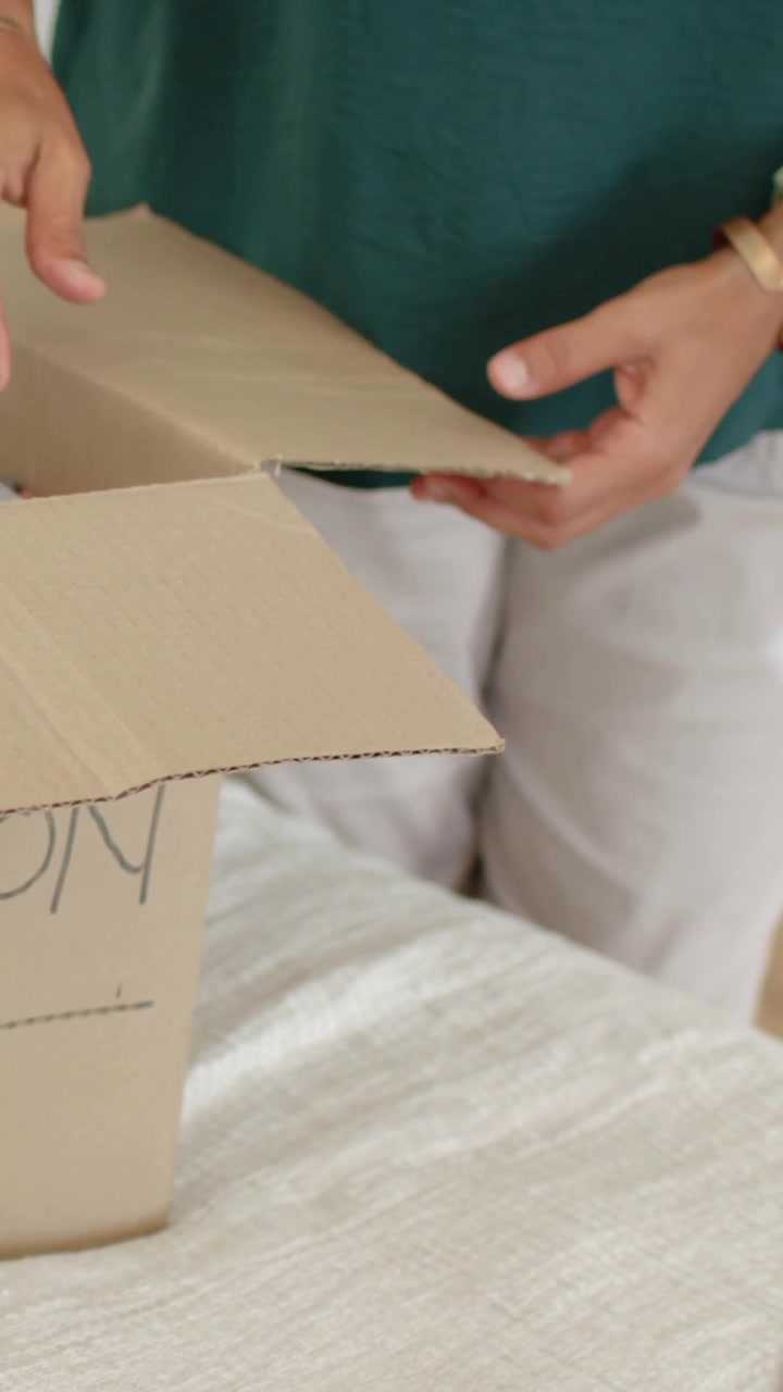 Vertical video: Folding flaps, woman green top and man packing labeled box on bed preparing move