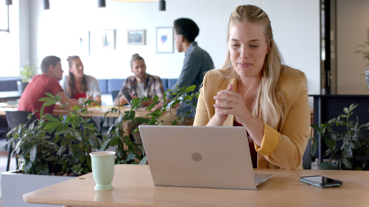 Glad, uformell forretningskvinne tar videosamtale på bærbar PC på kontoret, sakte film.
