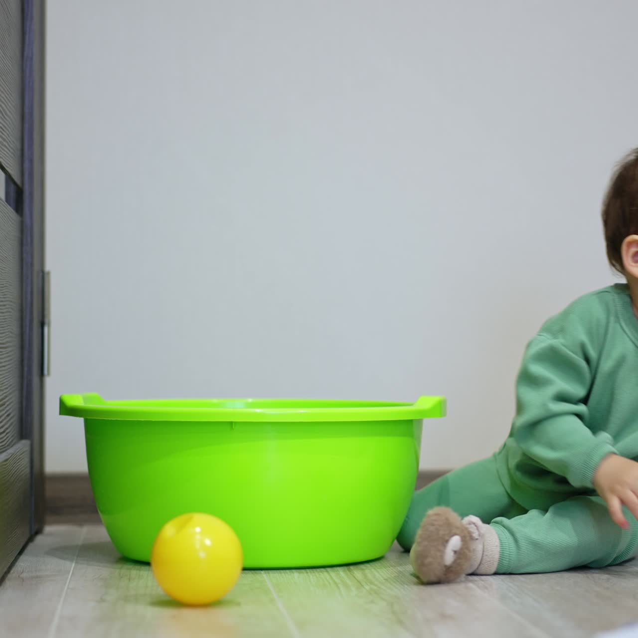Beautiful child trying to get into the washbowl but sits beside. Yellow ball is at the tub