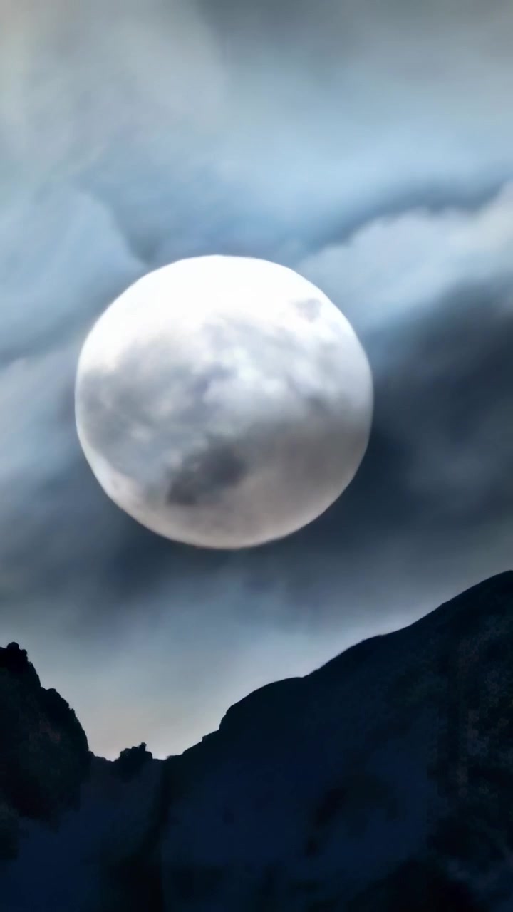 Video vertical: Viento empujando nubes a través de la luna llena sobre la cresta de una montaña, revelando su brillo menguante.
