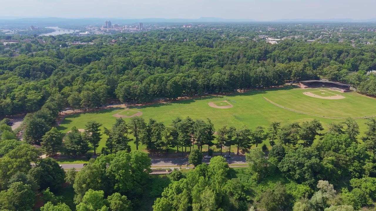 Vuelo panorámico de dron cerca de un campo deportivo rodeado de densos bosques en un área de recreación comunitaria con el horizonte distante de la ciudad de Springfield, Massachusetts, EE. UU.
