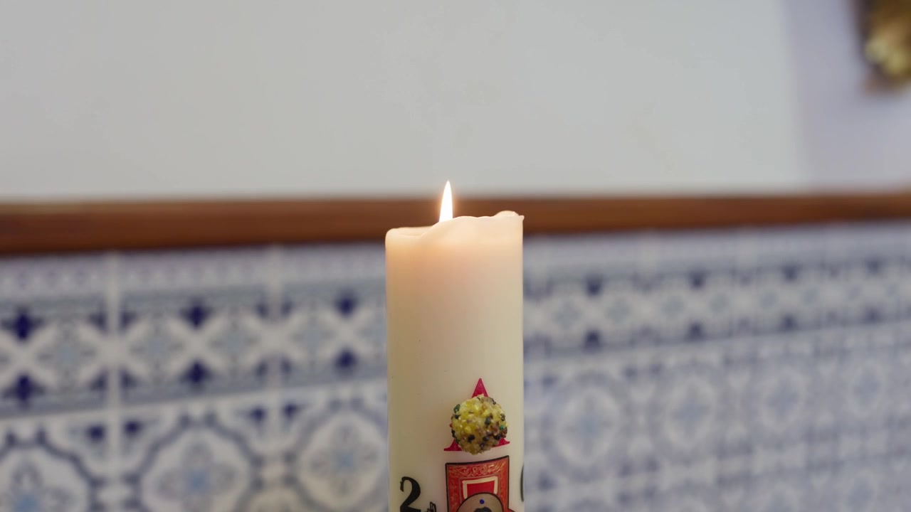 Vela blanca decorada encendida frente a azulejos azules en Portugal
