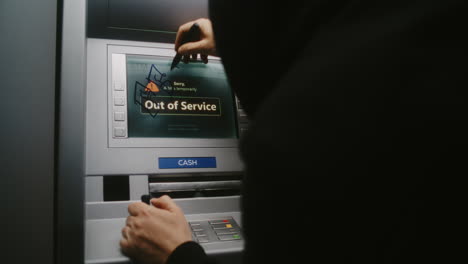 unrecognizable vandal in hoodie marking atm screen with graffiti using marker pen. person damaging property, vandalizing out of service cash machine with illegal graffiti. vandalism in public place.