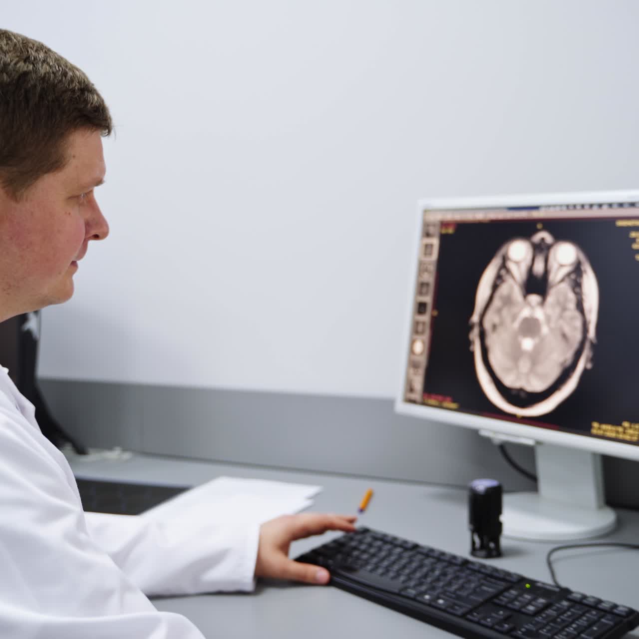 Tecnico di laboratorio concentrato osserva attentamente gli schermi dei suoi due computer. Professionista che digita la descrizione della scansione MRI e della diagnosi