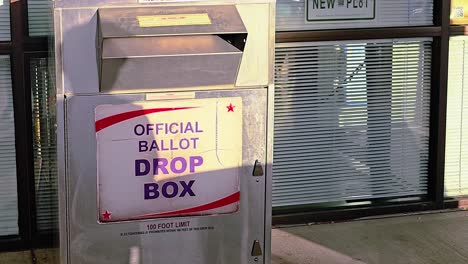 asian woman votes in election by dropping mail-in ballot letter in slot at voting booth with offical ballot drop box sign for democratic government campaign in presidential race