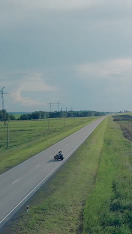 bird eye view couple on motorcycle lit by summer sunlight turns back and drives near pictorial green grass
