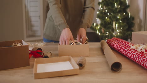 カメラは、クリスマス ツリー 1 で飾られた部屋のテーブルに女性の手のラッピング クリスマス プレゼントに焦点を当てる