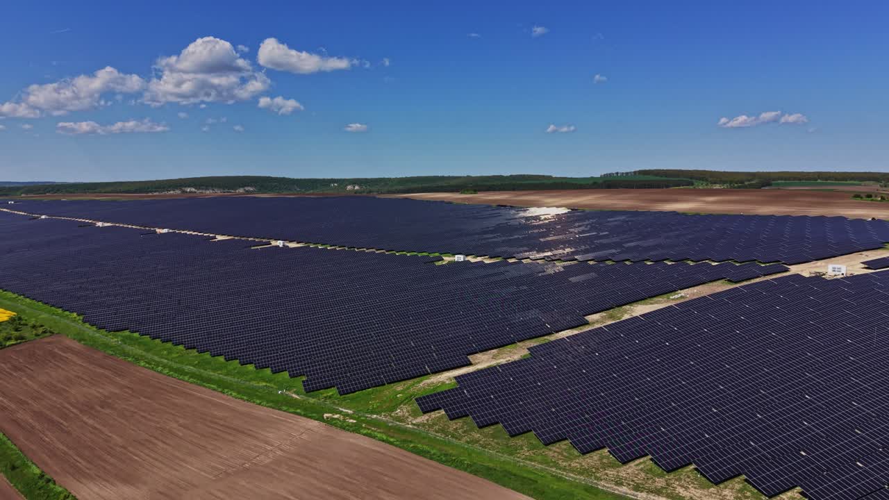Solpaneler dækker stort felt under blå himmel med skyer